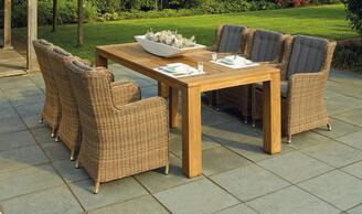 A concrete patio sits next to a mowed lawn. A posh outdoor table sits on the patio with set of six chairs. 