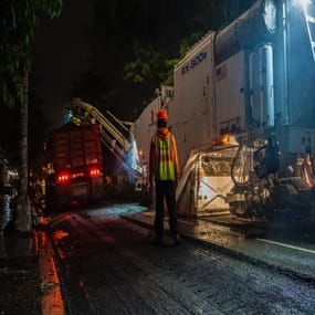 A night time concrete job takes place with heavy machinery. 