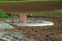 The base layer of a concrete foundation juts out of the ground with re-barb. 